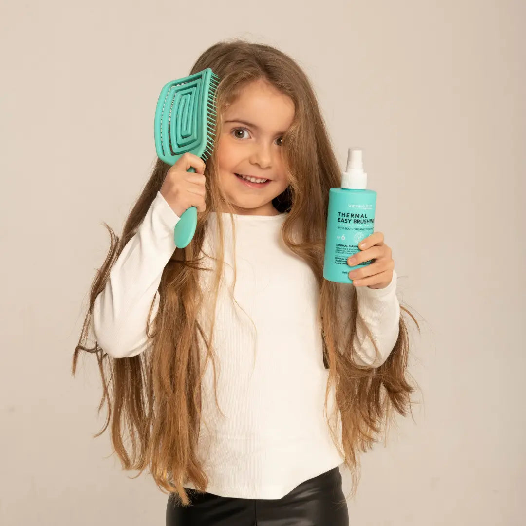 uśmiechnięta dziewczynka czesząca się szczotką i trzymająca w ręce Somnis&Hair - Spray Termoochronny - Thermal Easy Brushing nº6